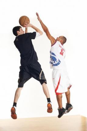 Two young men in basketball uniform playing basketball on white background.